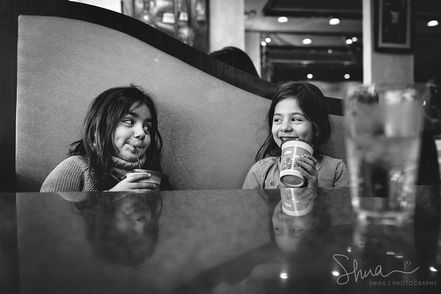 girls sitting at diner table in Long Island, NY smiling at each other